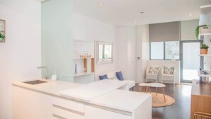 Eine moderne Küche mit weißen Schränken, einer zentralen Kochinsel und einem Essbereich mit weißen Stühlen und einem runden Tisch.