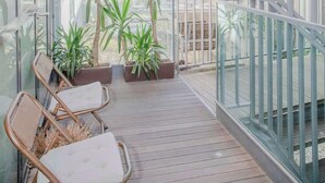 Ein Balkon mit Holzboden, Blumentöpfen und zwei Korbstühlen.