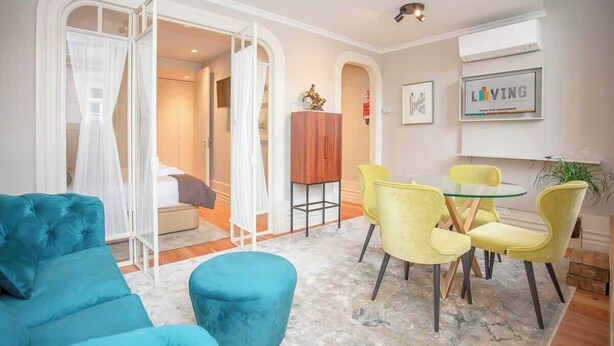 A modern living room with a teal sofa, a glass coffee table, and yellow chairs. There is a bed with a canopy in the background. - Liiiving in Porto - Cedofeita Charming Apartment (Porto)