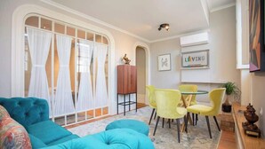 A living room with a teal sofa, yellow chairs, a small table, and a large window with white curtains. - Liiiving in Porto - Cedofeita Charming Apartment (Porto)