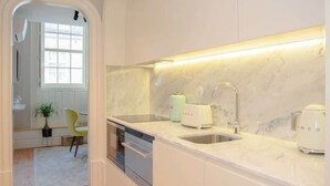 A modern kitchen with white cabinetry, a marble countertop, and built-in appliances. - Liiiving in Porto - Cedofeita Charming Apartment (Porto)