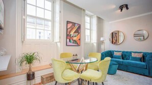 A modern living room with a glass-top dining table, yellow chairs, a blue sofa, and a large abstract painting on the wall. - Liiiving in Porto - Cedofeita Charming Apartment (Porto)