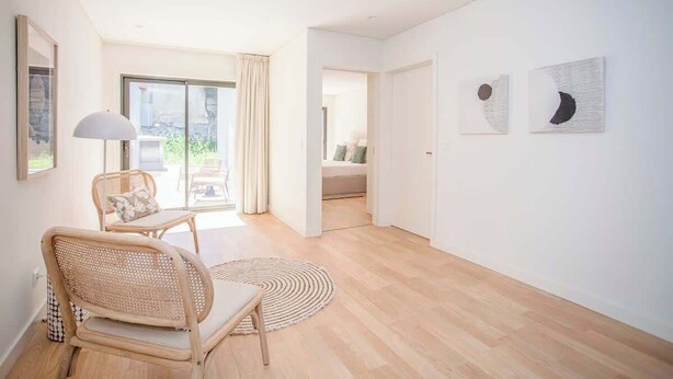 A spacious room with a wooden floor, a rattan chair, a round rug, and a large window with curtains. - Liiiving in Porto - City Design Apartment C (Porto)