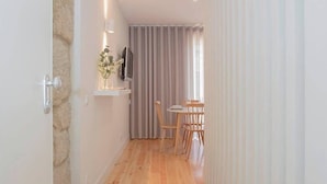 Un couloir étroit avec un plancher en bois, un coin repas avec une table et des chaises, et un téléviseur posé sur une étagère.
