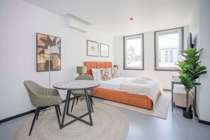 A modern hotel room with a bed, a round dining table, two chairs, a potted plant, and large windows. - Liiiving in Porto - City Design Studio I (Porto)