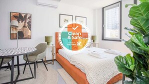 A modern hotel room with a bed, a round table, and chairs, a large window, and a plant.