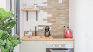 A compact kitchen with a built-in oven, a coffee maker, and a red kettle on the countertop.