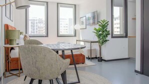 A modern living room with a round dining table, a comfortable armchair, a sofa, a lamp, a potted plant, and a TV.