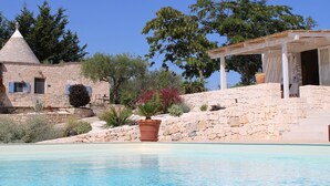 A pool with a stone wall and a building with a conical roof. - Stylishly restored trullo with private pool and stunning views (Martina Franca)