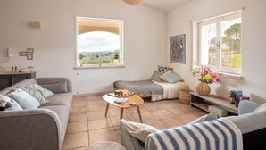 A living room with a sofa, a coffee table, and a bench. There is a window with a view of the countryside. - Stylishly restored trullo with private pool and stunning views (Martina Franca)