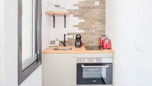 A compact kitchen with a built-in oven, a coffee maker, and a red kettle on the countertop. - Liiiving in Porto - City Design Studio II (Porto)