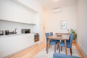 Une cuisine moderne avec des meubles blancs, une table à manger entourée de chaises bleues et une plante en pot.