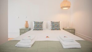 A neatly made bed with two pillows, a bedside lamp, and a vase on a nightstand. - Liiiving in Porto - Downtown Balcony Studio (Porto)