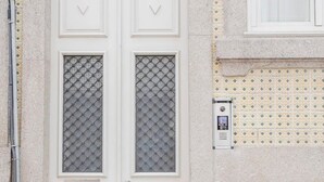 A white double door with a number plate, a decorative metal grille, and a small window with a metal grill. - Liiiving in Porto - Downtown Balcony Studio (Porto)