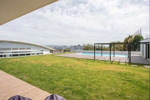 A modern outdoor area with a swimming pool, a grassy lawn, and a view of a cityscape.