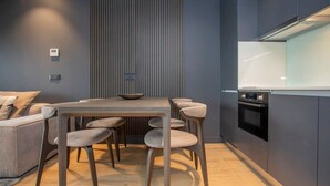 A modern kitchen with a dark grey color scheme, a wooden dining table with six chairs, and a built-in oven. - Liiiving in Porto - Dragão Pool View (Porto)