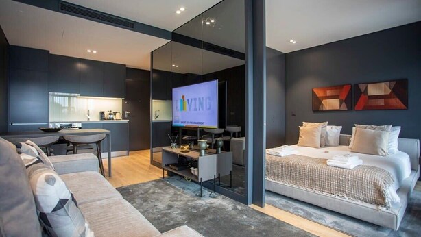 A modern hotel room with a sofa, a bed, a TV, and a kitchen area. - Liiiving in Porto - Dragão Pool View (Porto)