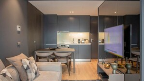 A modern living room with a sofa, a coffee table, and a TV. There is a kitchen in the background with a dining area. - Liiiving in Porto - Dragão Pool View (Porto)