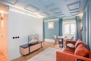 Uma sala de estar moderna com sofá, televisão em móvel, área de jantar com mesa e cadeiras, e janela com cortinas.