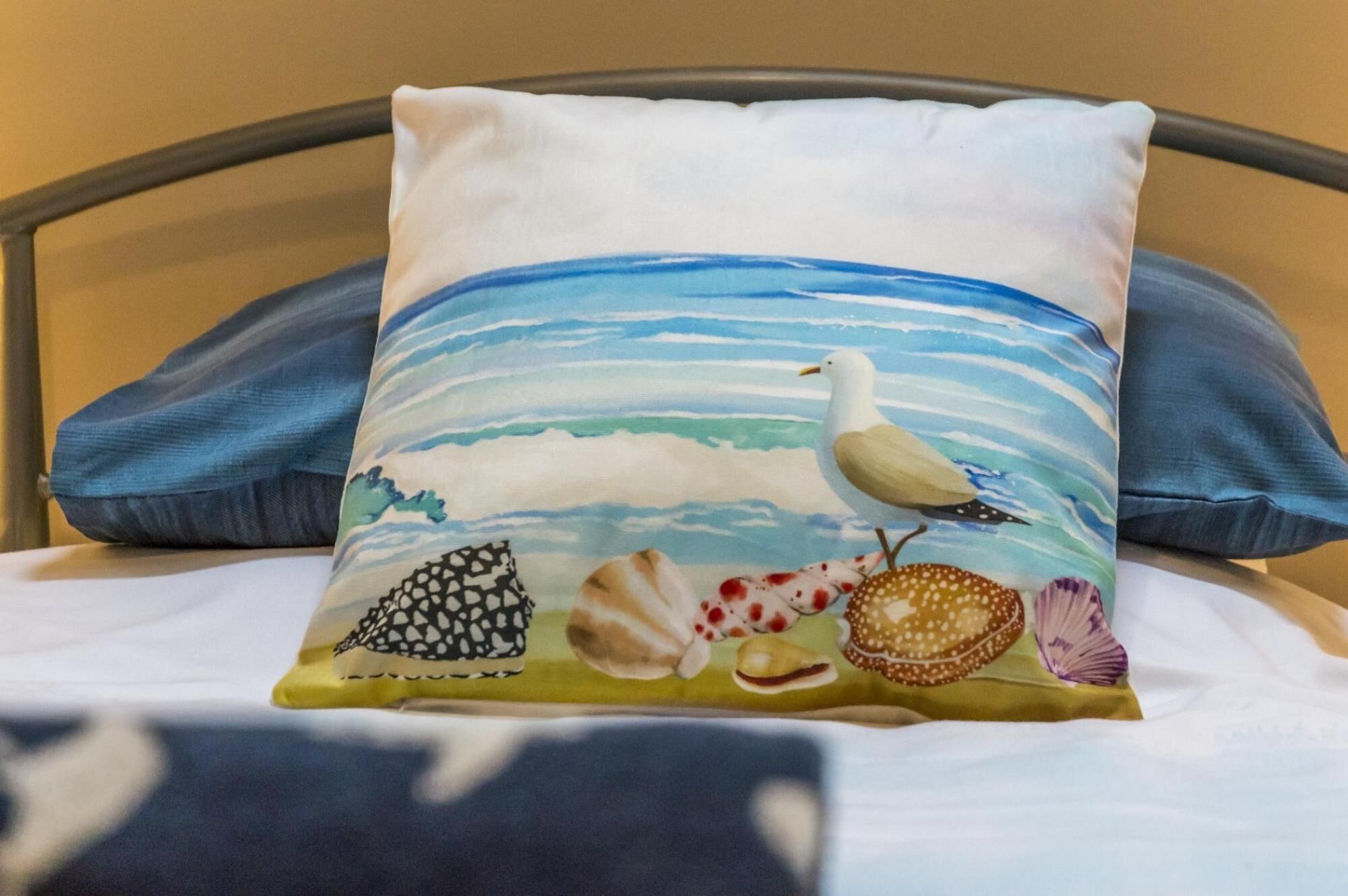 Una cama con un almohadón que muestra una gaviota y conchas marinas.