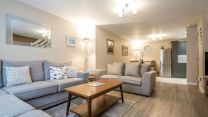 A modern living room with a grey sofa set, a wooden coffee table, and a dining area with a chandelier. - Harry s - 2 Bedroom Holiday Home - Tenby (Tenby)