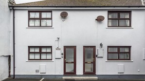A two-story building with a white facade, a central entrance with a glass door, and multiple windows with brown frames. - Harry s - 2 Bedroom Holiday Home - Tenby (Tenby)