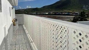 En balkong med ett vitt, gallerverksliknande räcke som vetter ut mot ett kustområde med ett berg i bakgrunden.