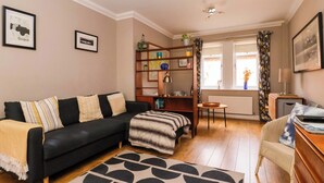Ein modernes Wohnzimmer mit einer schwarzen Couch, einem gemusterten Teppich, einem Holztisch und einem Bücherregal.