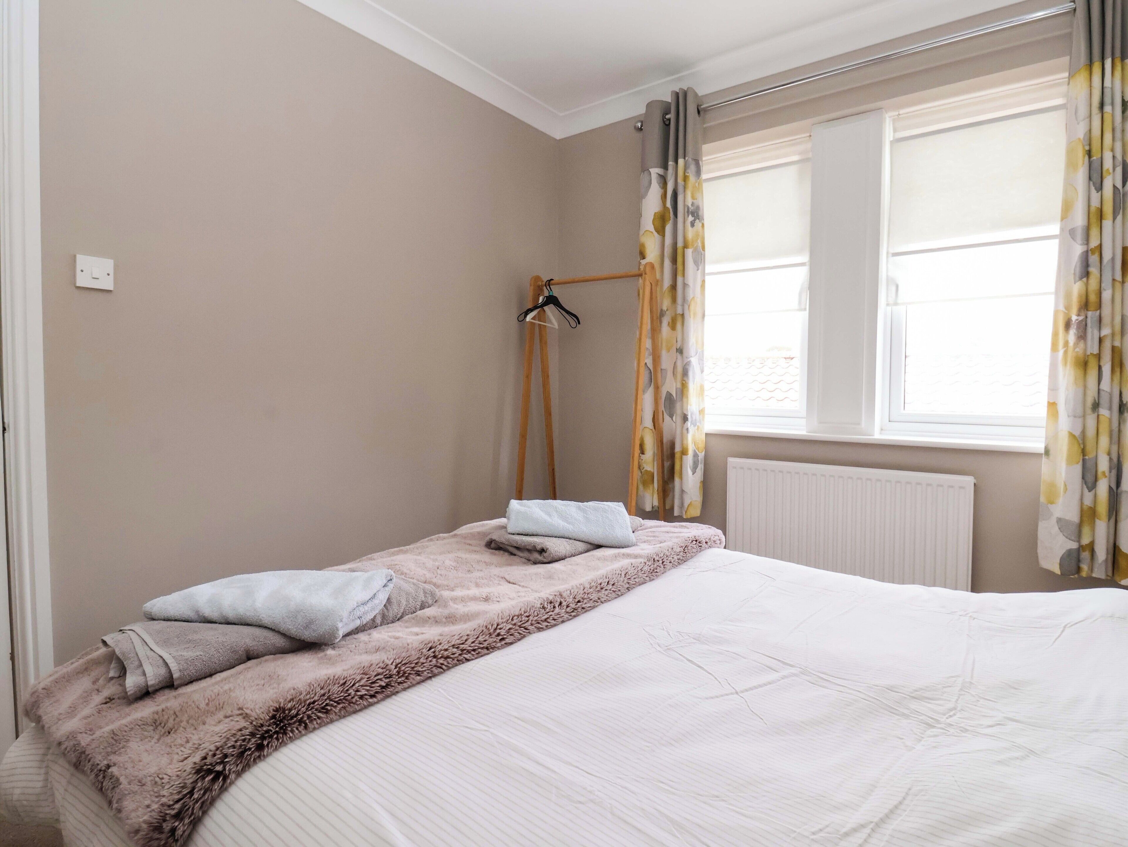 A bedroom with a bed, a radiator, a window with curtains, and a towel rack.