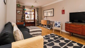 Ein Wohnzimmer mit einer Couch, einem Sessel, einem Fernseher, einem Bücherregal und einem Schreibtisch.