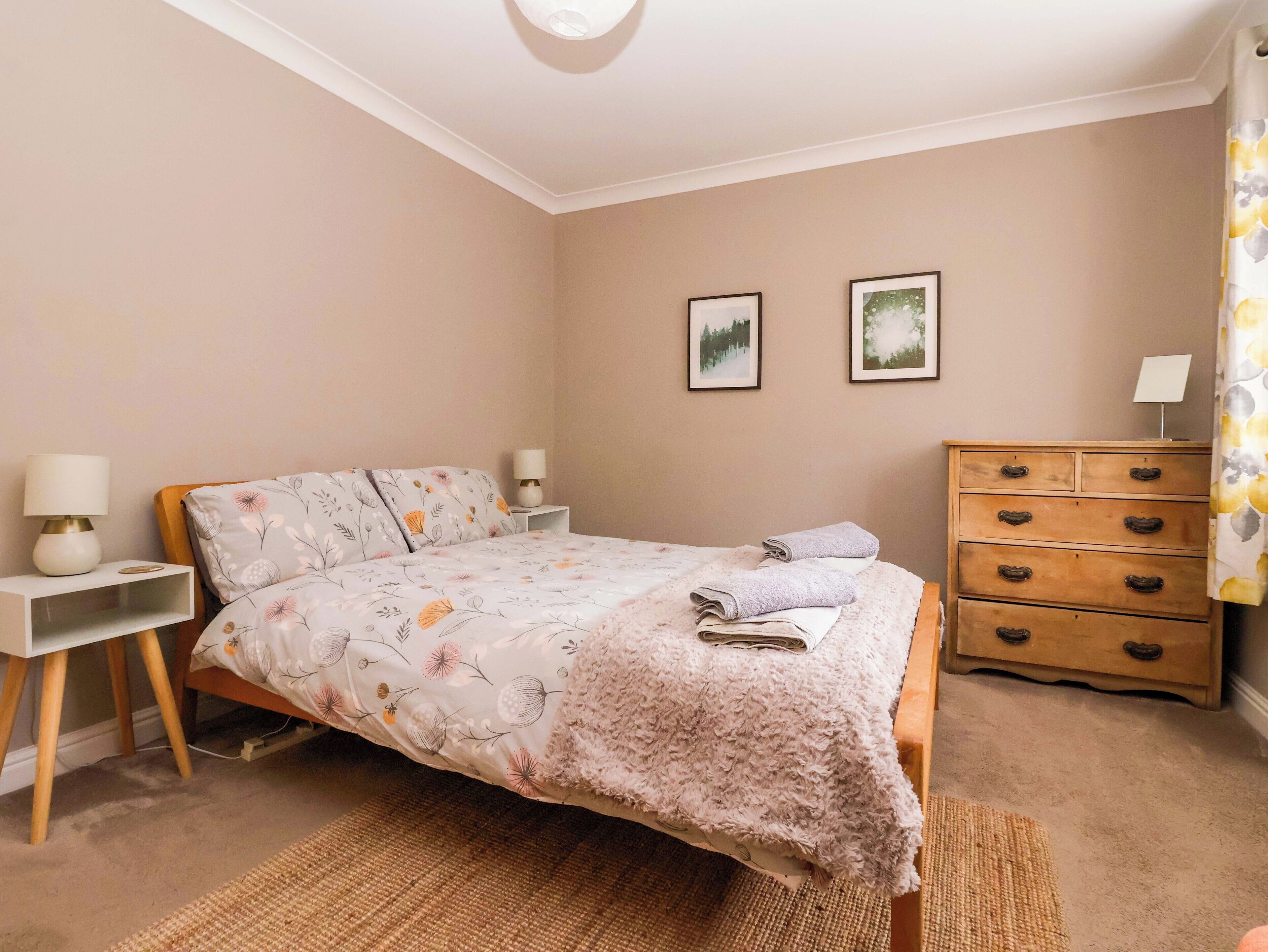 A bedroom with a bed, bedside tables, a dresser, and two framed pictures on the wall.