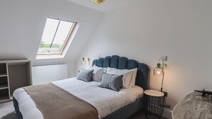 Une chambre à coucher moderne avec un grand lit, une lucarne, une table de chevet et une table ronde.