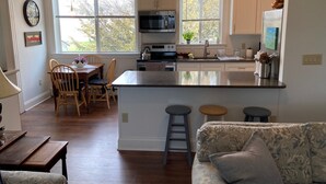 Une cuisine spacieuse dotée d’un îlot central, d’une table à manger en bois et de chaises. Deux fenêtres laissent entrer la lumière naturelle.
