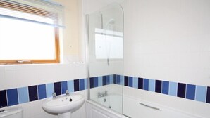 Kylpyhuone, jossa on valkoinen pesuallas, wc, lasiseinällä varustettu suihku ja kylpyamme.