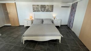 A bedroom with a large bed, two bedside tables, a wall-mounted artwork, and a door on the left. - 5 min from Orient Bay-magical view (Collectivity of Saint Martin)