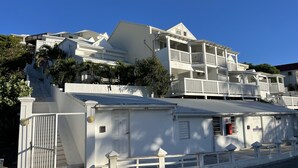 A multi-story white building with balconies, a gated entrance, and a staircase leading to the upper floors. - 5 min from Orient Bay-magical view (Collectivity of Saint Martin)