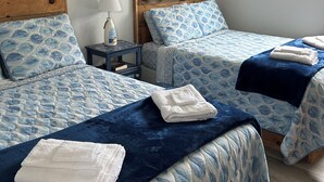 Een hotelkamer met twee bedden, elk met een blauw bedlaken met dessin en passende kussens. Er is een nachtkastje met een lamp en een klein tafeltje met een vaas.