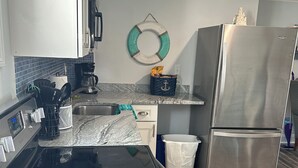 Een keuken met een zwarte kookplaat, een roestvrijstalen koelkast en een blauwe mand met een anker dessin op het aanrecht.