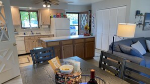 A modern kitchen with wooden cabinets, a dining table with chairs, and a living area with a sofa and a lamp. - “Stay Anchored” Lake Tippecanoe channel front with pier and great lake views (Leesburg)
