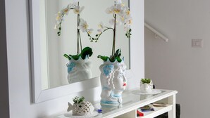 Un tavolo consolle bianco con uno specchio sopra, che riflette orchidee bianche e un vaso bianco con un motivo blu.