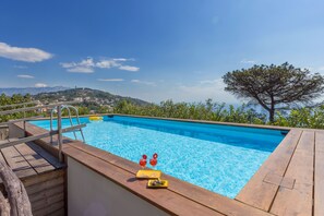 Une piscine avec une terrasse en bois, une échelle et une vue sur une montagne et des arbres.