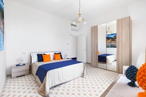Une chambre à coucher moderne, avec un lit, des tables de chevet, un miroir et une vue sur un paysage côtier.