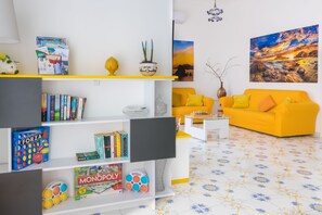 A living room with a yellow sofa, a bookshelf with board games, and a painting on the wall. - Villa Fedora, with private pool, between Sorrento and Amalfi Coast (Massa Lubrense)