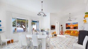 Un soggiorno moderno con un divano bianco, un tavolo da pranzo con sedie, una TV e un quadro appeso al muro.