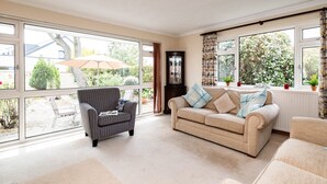A spacious living room with large windows, a sofa, a chair, and a cabinet. - Longhouse Bungalow (Wadebridge)