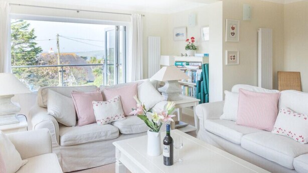 A bright living room with white sofas, a coffee table with a bottle and glass, and a bookshelf.