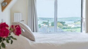 A bedroom with a large bed, a view of the sea, and a window with curtains.