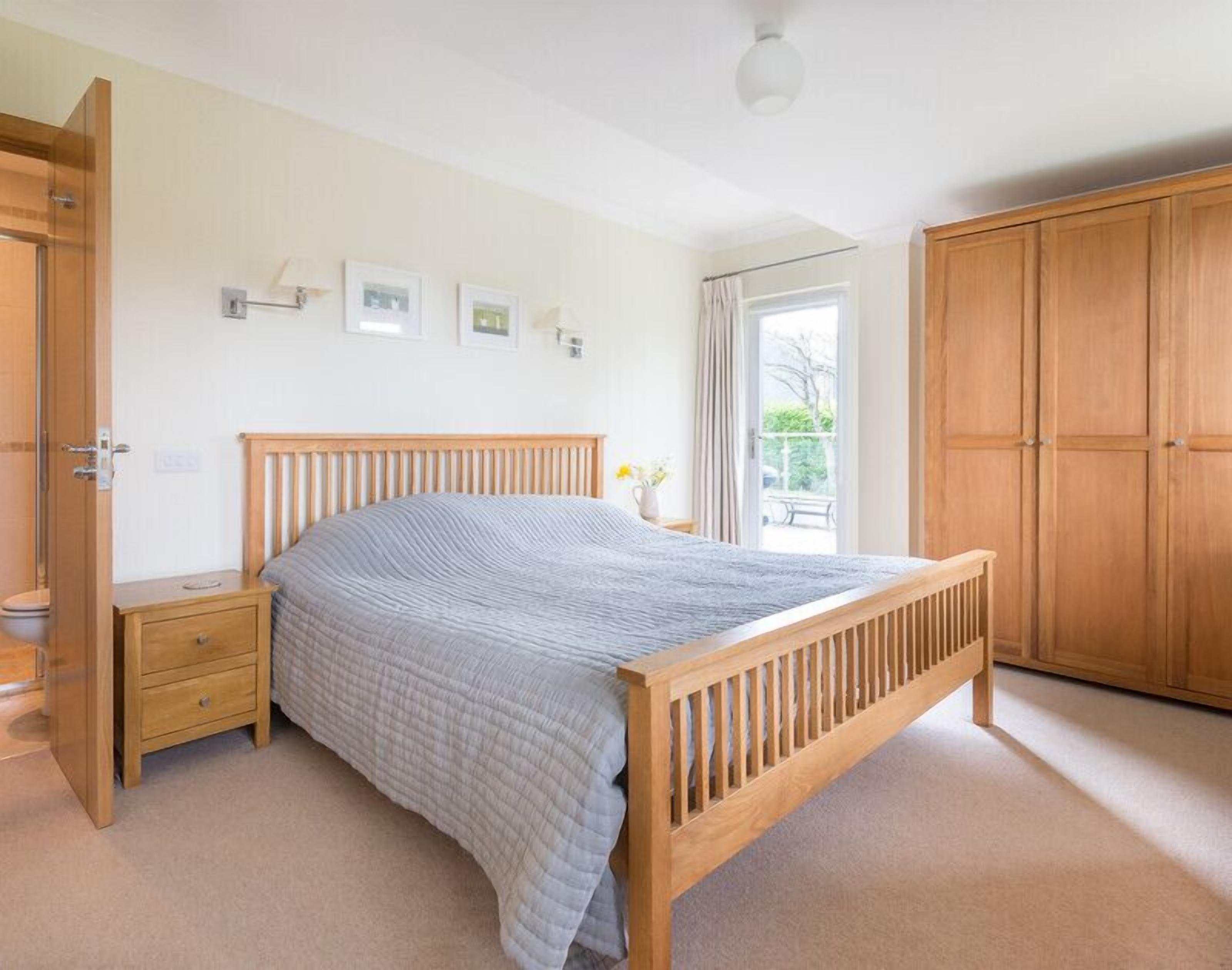 A bedroom with a wooden bed, a nightstand, a wardrobe, and a window with curtains.