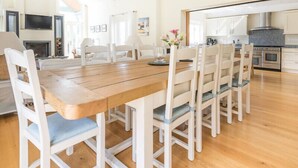 A spacious dining area with a wooden table and white chairs, a kitchen with modern appliances, and a high ceiling with exposed beams.