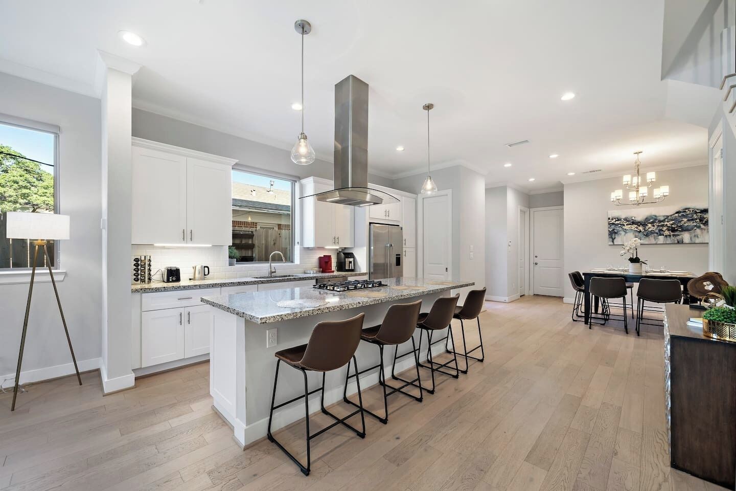 A modern kitchen with a central island, bar stools, and a dining area with a chandelier.